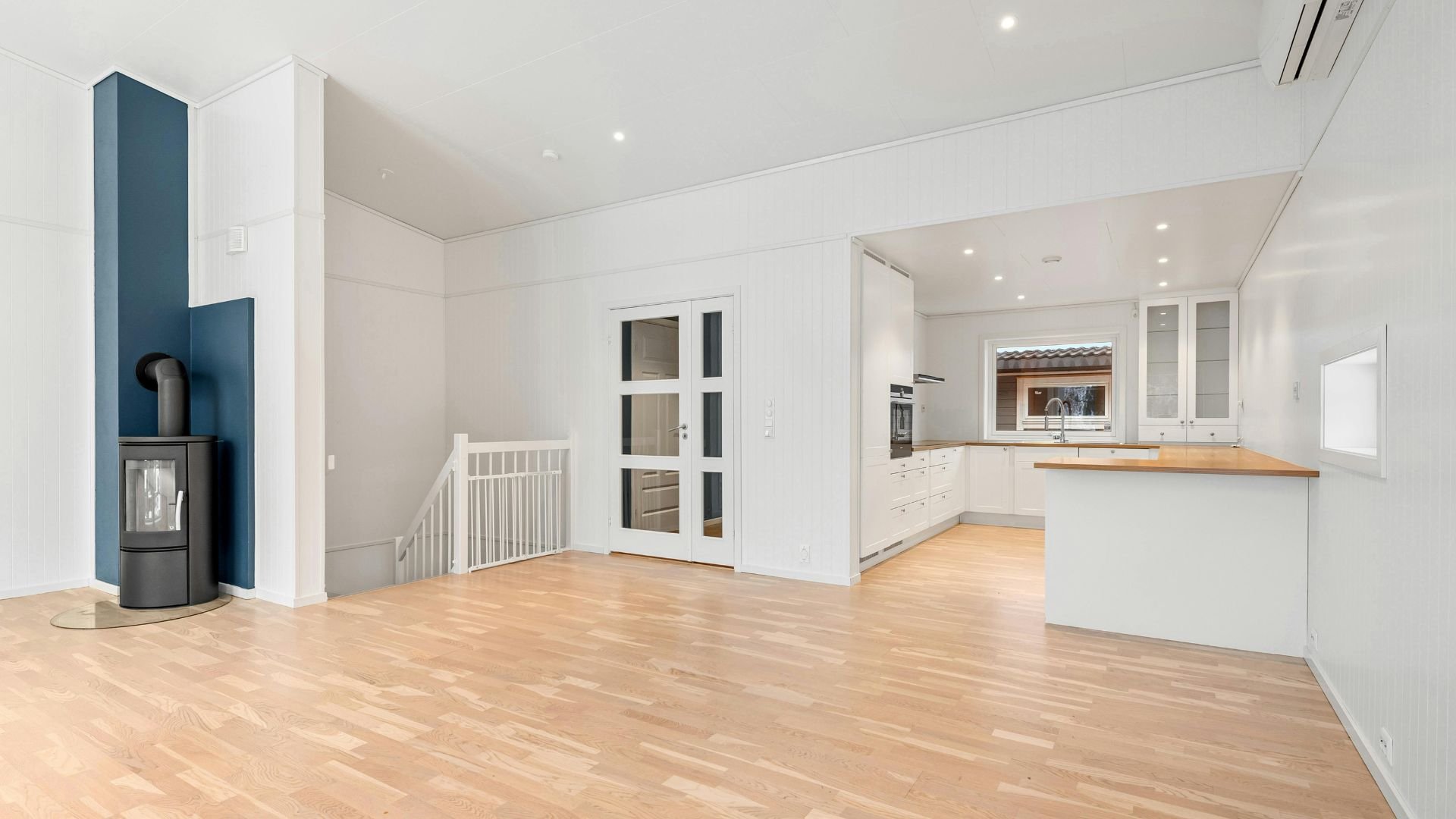 Modern, bright interior with wood floor, blue accent wall, and open kitchen