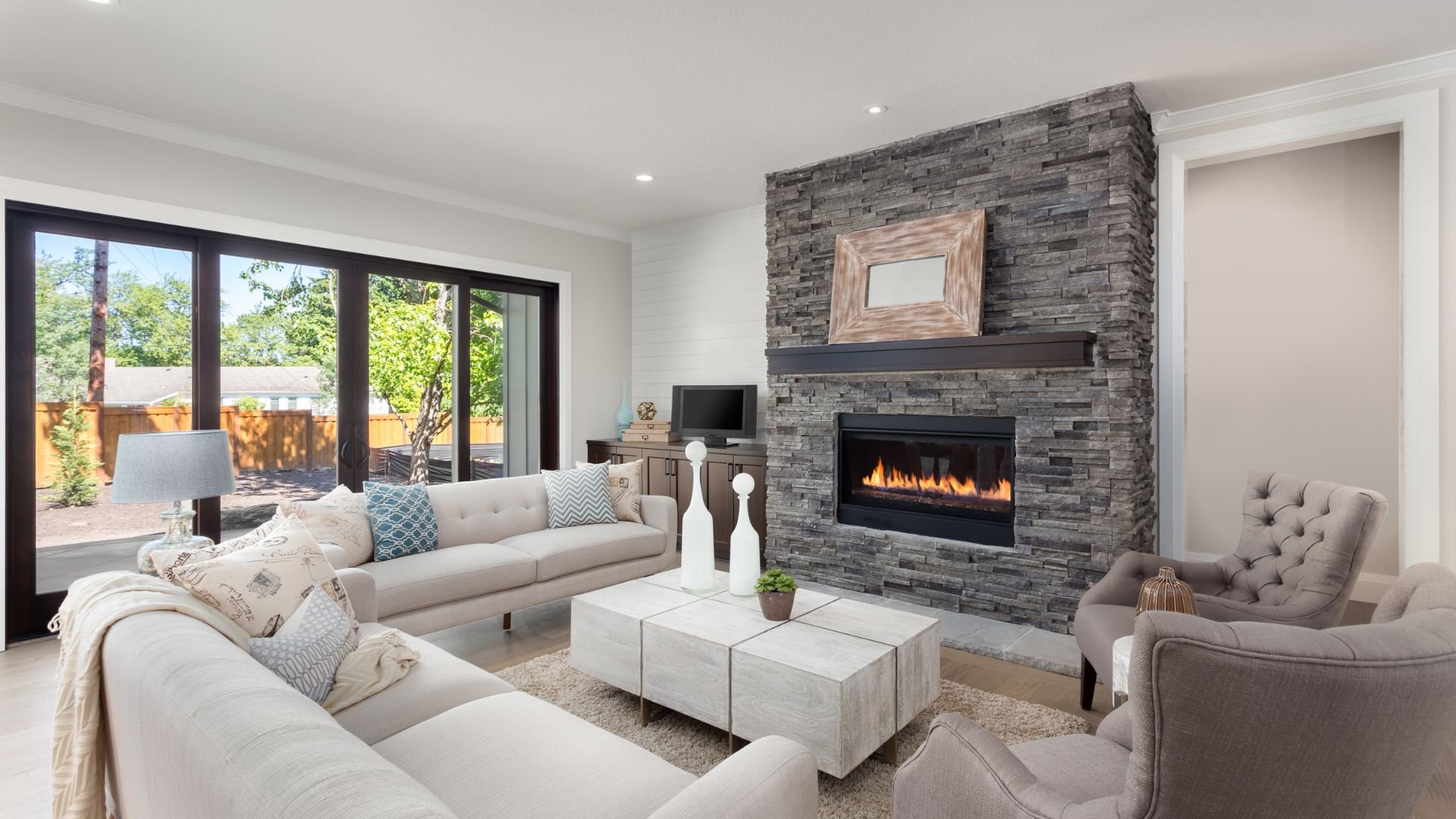 Modern living room with stone fireplace, large windows, and cozy furniture