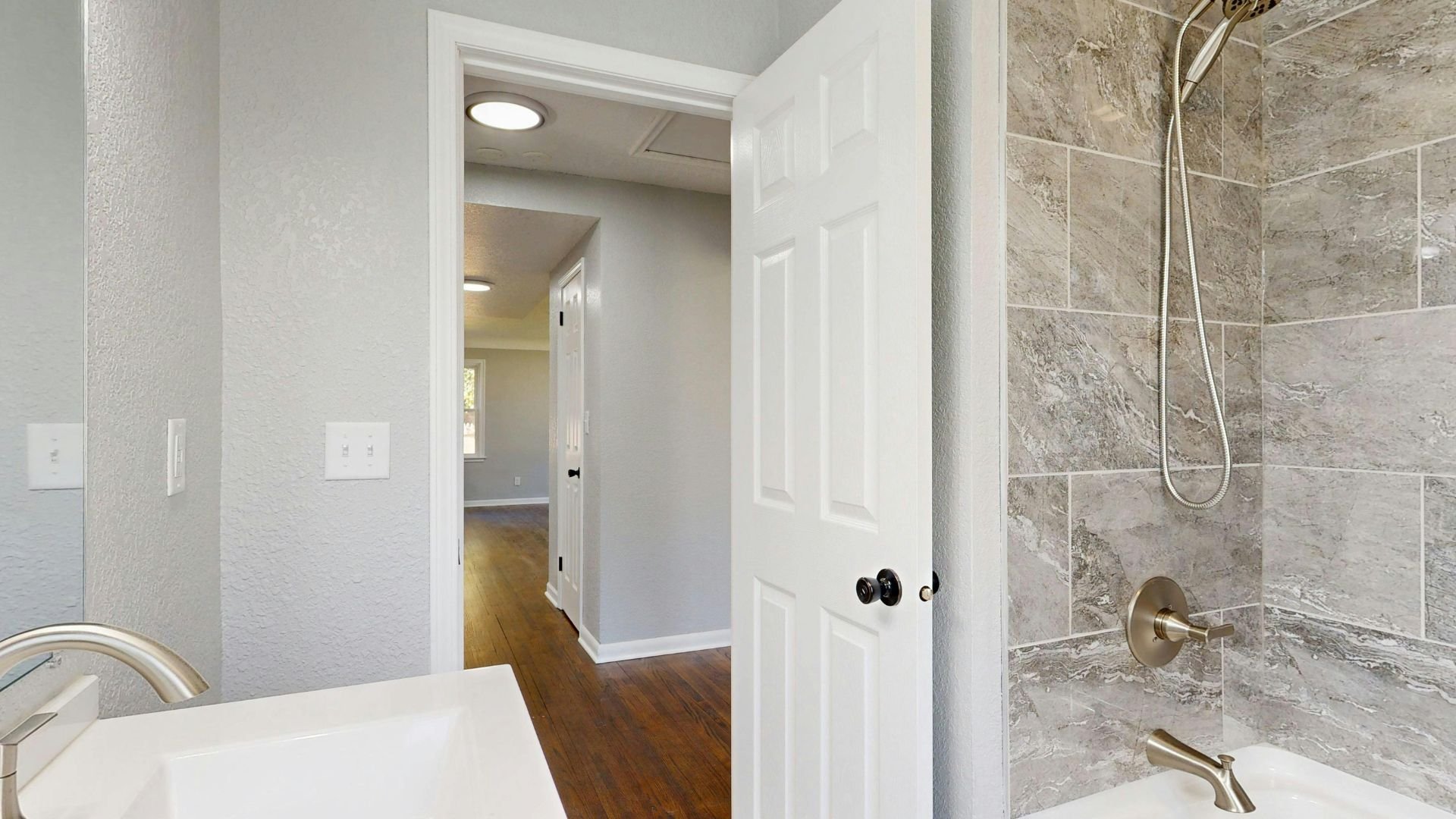 Open white bathroom door revealing hallway with wooden floor